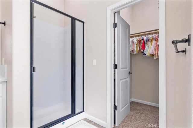 full bathroom with baseboards, a spacious closet, and a stall shower