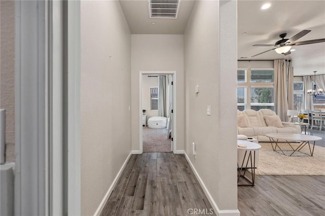 hall featuring a textured wall, visible vents, baseboards, wood finished floors, and a notable chandelier
