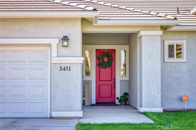 view of exterior entry with a tile roof, stucco siding, and an attached garage