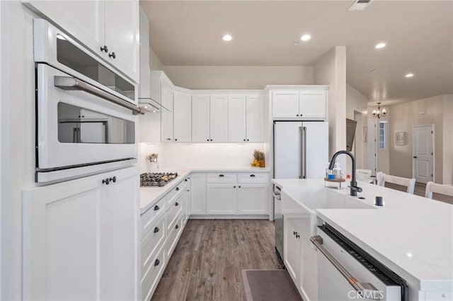 kitchen with an inviting chandelier, white appliances, white cabinetry, light countertops, and an island with sink