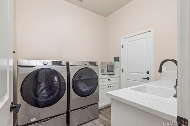 clothes washing area with washer and clothes dryer, light wood-style floors, laundry area, and a sink