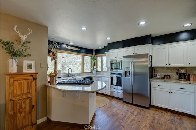 kitchen featuring light stone countertops, appliances with stainless steel finishes, a warming drawer, dark wood-style floors, and a peninsula