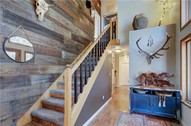 stairway featuring baseboards, wood walls, wood finished floors, and a towering ceiling