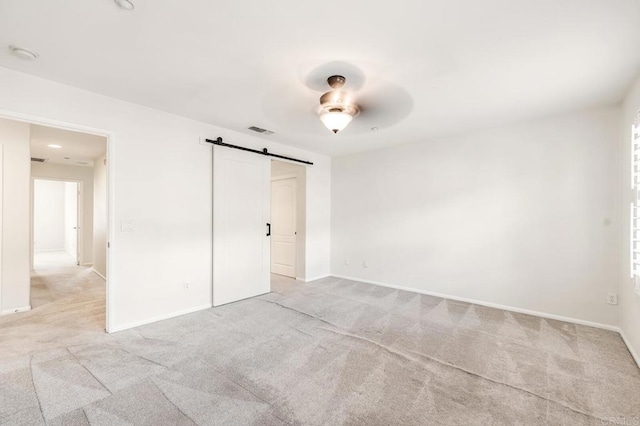 unfurnished bedroom featuring baseboards, light colored carpet, a barn door, and visible vents