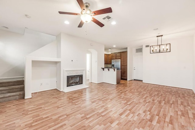 unfurnished living room featuring ceiling fan with notable chandelier, light wood finished floors, stairs, and visible vents