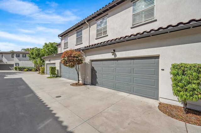 view of side of property with concrete driveway, an attached garage, a tile roof, and stucco siding