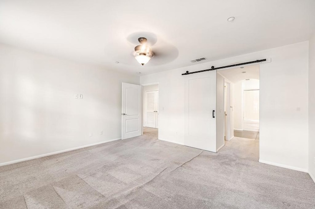 unfurnished bedroom with a ceiling fan, visible vents, a barn door, baseboards, and light carpet
