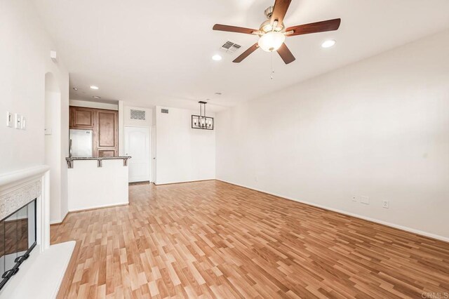 unfurnished living room featuring visible vents, a glass covered fireplace, recessed lighting, light wood finished floors, and ceiling fan with notable chandelier