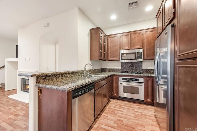 kitchen with visible vents, light wood-style flooring, a sink, dark stone countertops, and stainless steel appliances