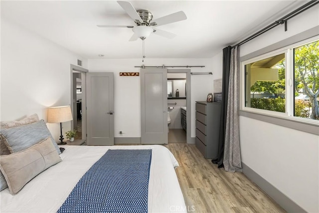 bedroom featuring connected bathroom, light wood-style flooring, a barn door, visible vents, and a ceiling fan