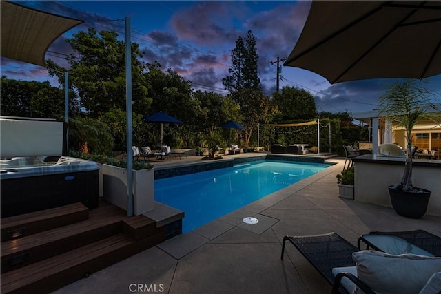 pool at dusk with an outdoor pool, a patio area, and a hot tub