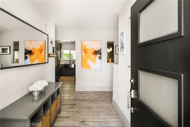 hall featuring wood finished floors, baseboards, visible vents, and a sink