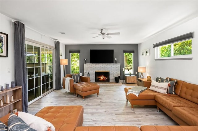living room featuring visible vents, ceiling fan, light wood-style flooring, and a brick fireplace