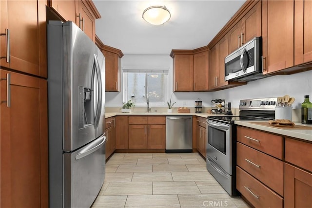 kitchen with light countertops, appliances with stainless steel finishes, brown cabinets, and a sink