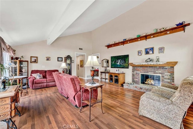 living area with a fireplace, visible vents, vaulted ceiling with beams, and wood finished floors