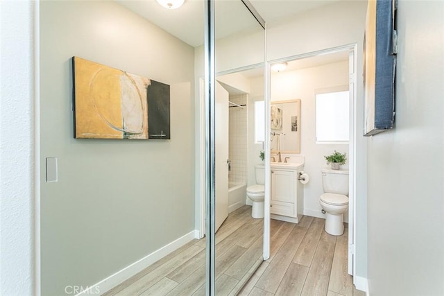 bathroom with wood finished floors, vanity, baseboards, toilet, and  shower combination