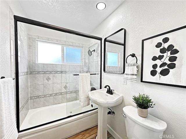 bathroom with a textured wall, wood finished floors, shower / bath combination with glass door, toilet, and a textured ceiling