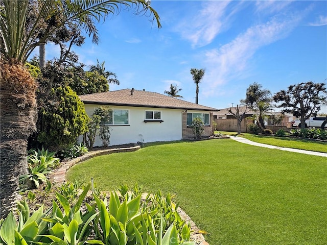 rear view of property with stucco siding, a yard, and fence