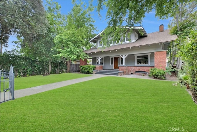view of front facade featuring a porch, a front yard, brick siding, a chimney, and fence