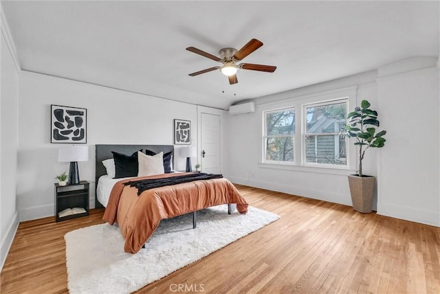 bedroom with light wood-type flooring, a ceiling fan, a wall mounted AC, and baseboards