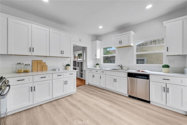 kitchen featuring stainless steel appliances, light countertops, white cabinets, light wood finished floors, and a sink