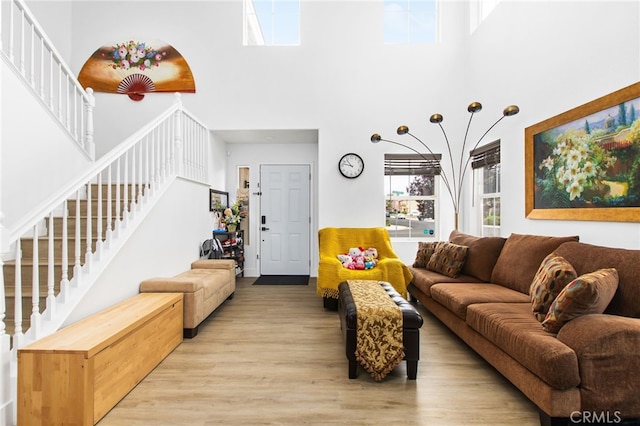living room featuring a towering ceiling, light wood-style floors, and stairway