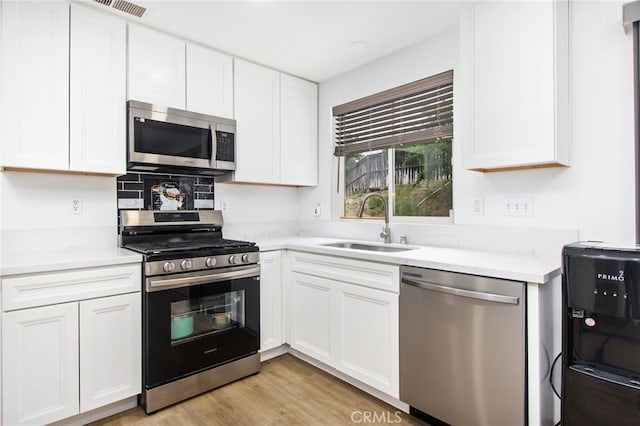 kitchen with light stone countertops, appliances with stainless steel finishes, a sink, white cabinetry, and light wood-type flooring