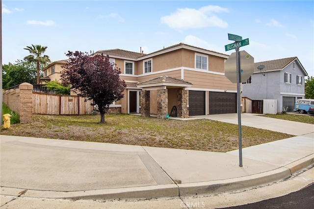 traditional-style home featuring an attached garage, stone siding, concrete driveway, stucco siding, and fence