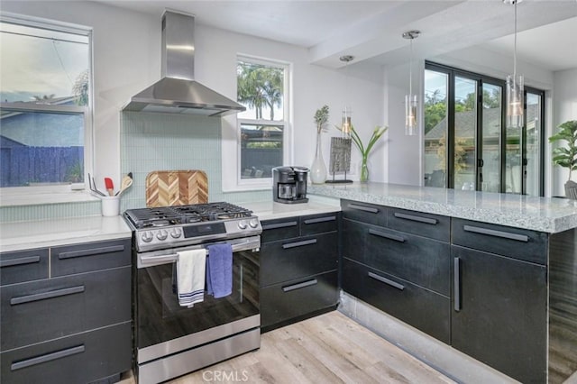 kitchen featuring decorative backsplash, wall chimney range hood, stainless steel gas range, light wood-type flooring, and dark cabinetry