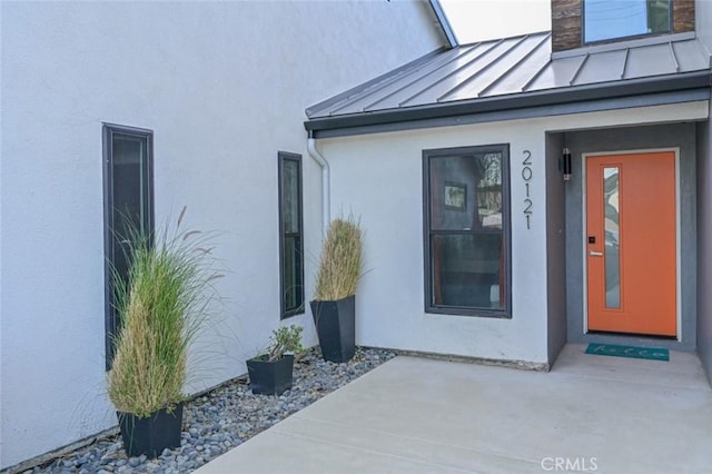 view of exterior entry featuring a standing seam roof, metal roof, a patio area, and stucco siding