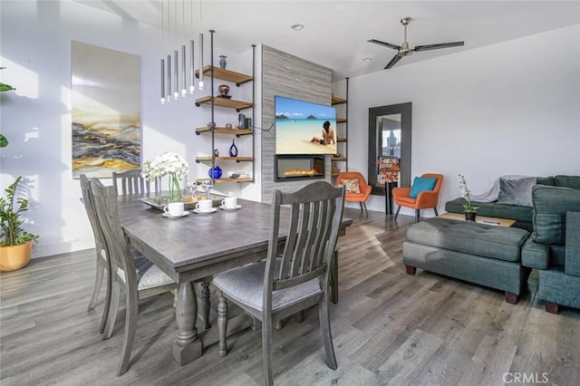 dining space featuring ceiling fan, a large fireplace, baseboards, and light wood-type flooring