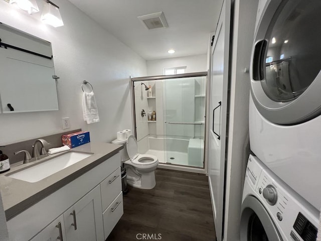 full bath with a stall shower, wood finished floors, stacked washing maching and dryer, vanity, and toilet