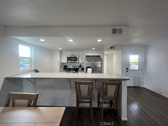 kitchen featuring white cabinets, a kitchen breakfast bar, appliances with stainless steel finishes, and visible vents