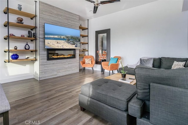 living area with baseboards, a ceiling fan, wood finished floors, and a fireplace
