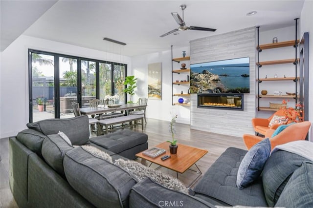 living room with a fireplace, a ceiling fan, and wood finished floors
