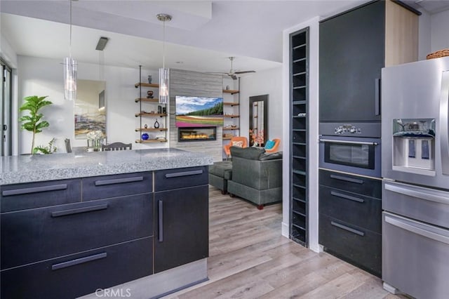 kitchen featuring stainless steel fridge with ice dispenser, light stone counters, light wood finished floors, a glass covered fireplace, and oven