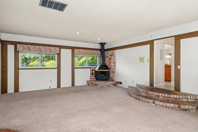 unfurnished living room with a wood stove, a wealth of natural light, carpet flooring, and visible vents