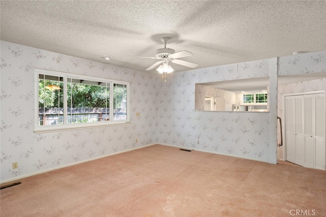 carpeted spare room featuring wallpapered walls, visible vents, and ceiling fan
