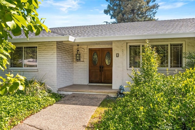 doorway to property featuring a shingled roof and brick siding