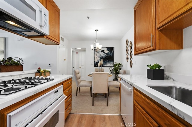 kitchen featuring white appliances, a chandelier, light wood-style flooring, brown cabinetry, and light stone countertops
