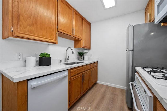 kitchen with white appliances, a sink, light wood-type flooring, and brown cabinets