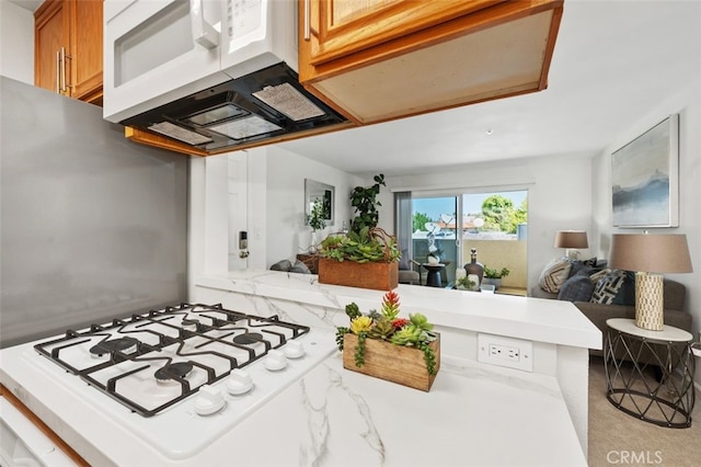 kitchen featuring white stovetop, brown cabinetry, open floor plan, ventilation hood, and a peninsula