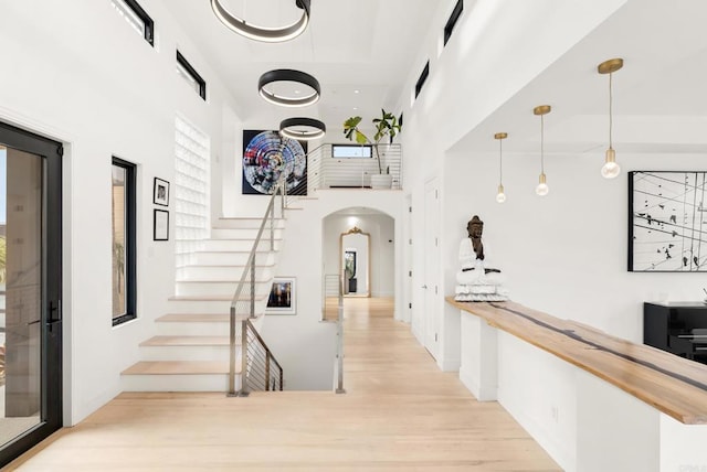 hall featuring light wood-type flooring, arched walkways, a high ceiling, and stairway