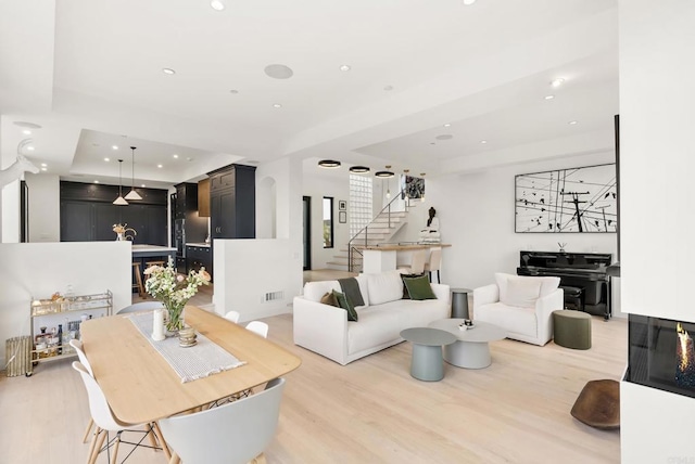 living area with recessed lighting, light wood-type flooring, a tray ceiling, stairs, and visible vents