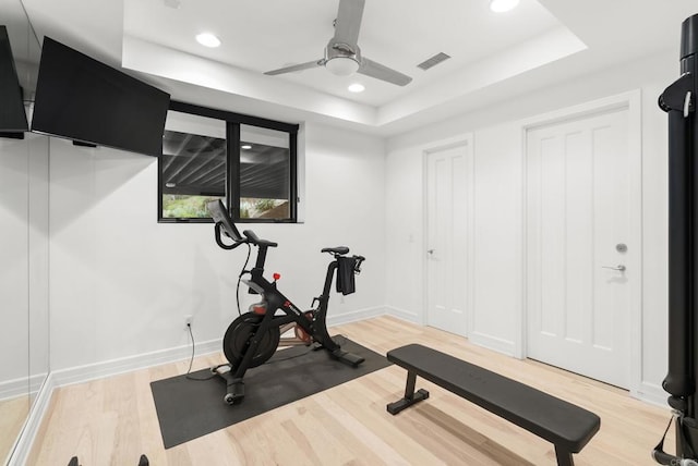 exercise room with visible vents, light wood-style floors, ceiling fan, a tray ceiling, and recessed lighting