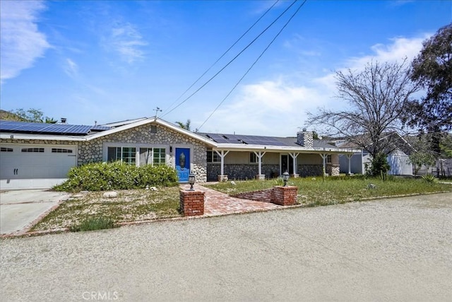 ranch-style house featuring driveway, stone siding, and solar panels