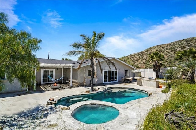 rear view of property featuring an in ground hot tub, an outdoor pool, a patio area, a mountain view, and stucco siding
