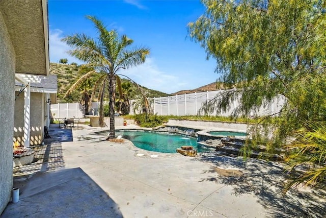 view of pool featuring a fenced backyard, a pool with connected hot tub, a mountain view, and a patio area