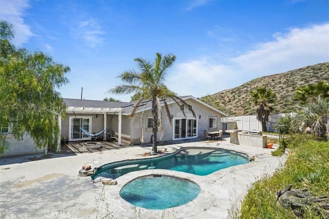rear view of property with a patio, an in ground hot tub, a mountain view, and stucco siding
