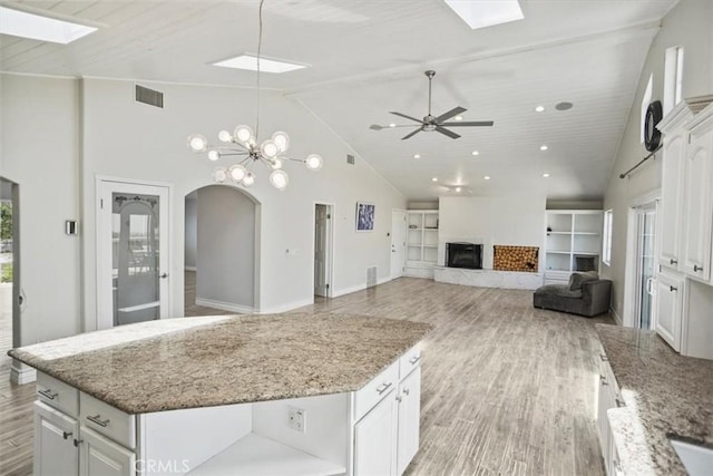 kitchen featuring a skylight, high vaulted ceiling, a fireplace with raised hearth, and light wood-style flooring